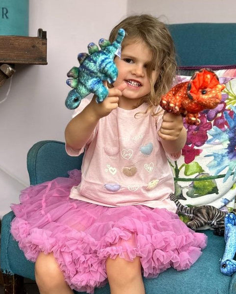 Child in a pink dress holding colourful dinosaur toys on a blue chair