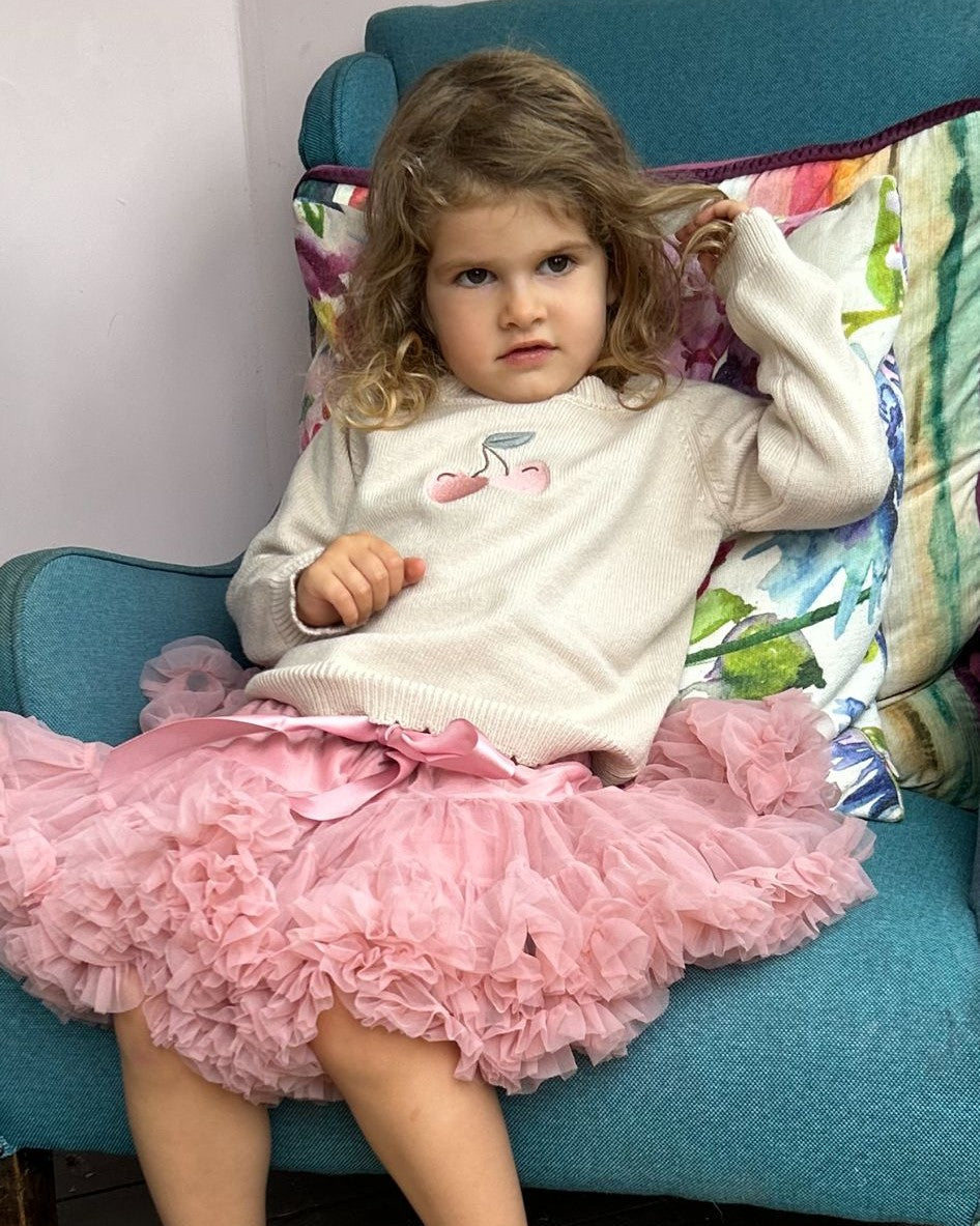 Young girl in a pink tulle skirt and white sweater sitting on a blue couch.