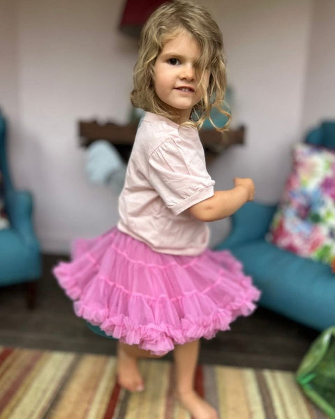 Child wearing a pink tutu skirt in a living room setting